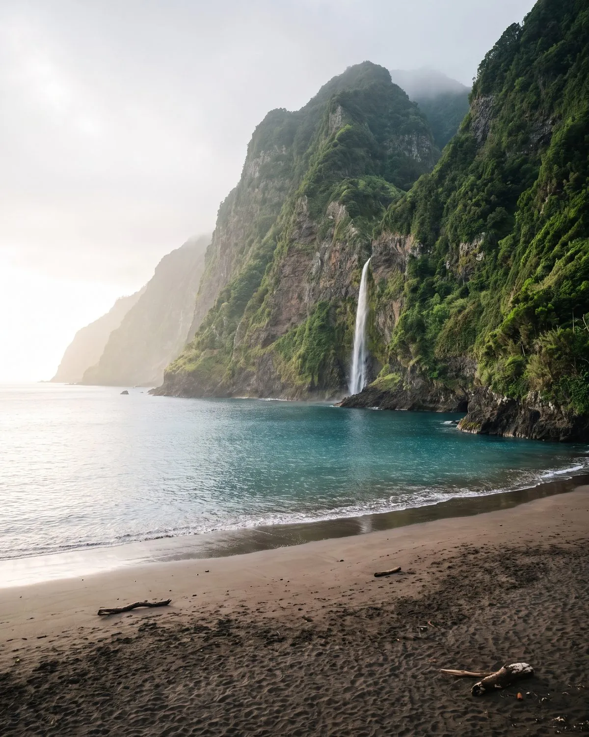 Black sand beach at Seixal under green cliffs with a waterfall